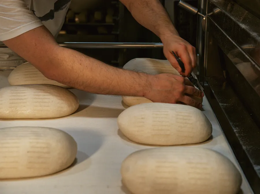A baker drawing loaves from a deck oven