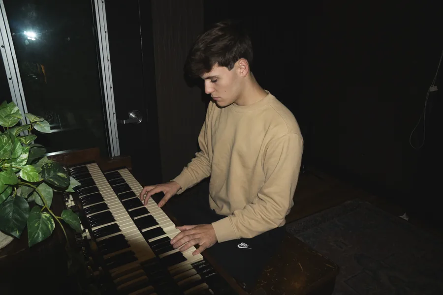 Playing a keyboard by a window, plants beside him