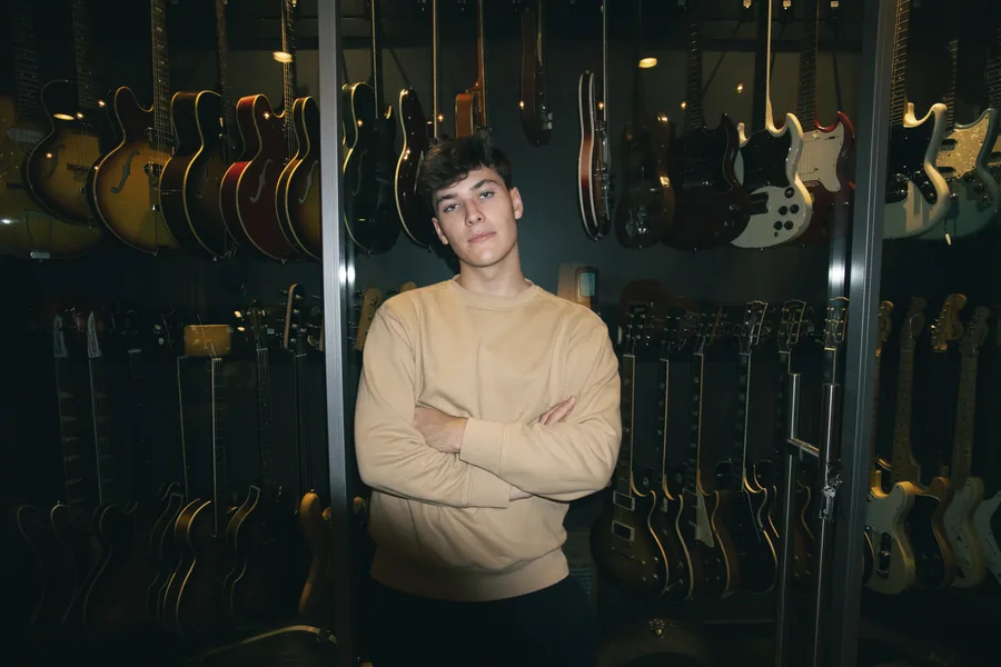 Arms folded in front of a wall of guitars