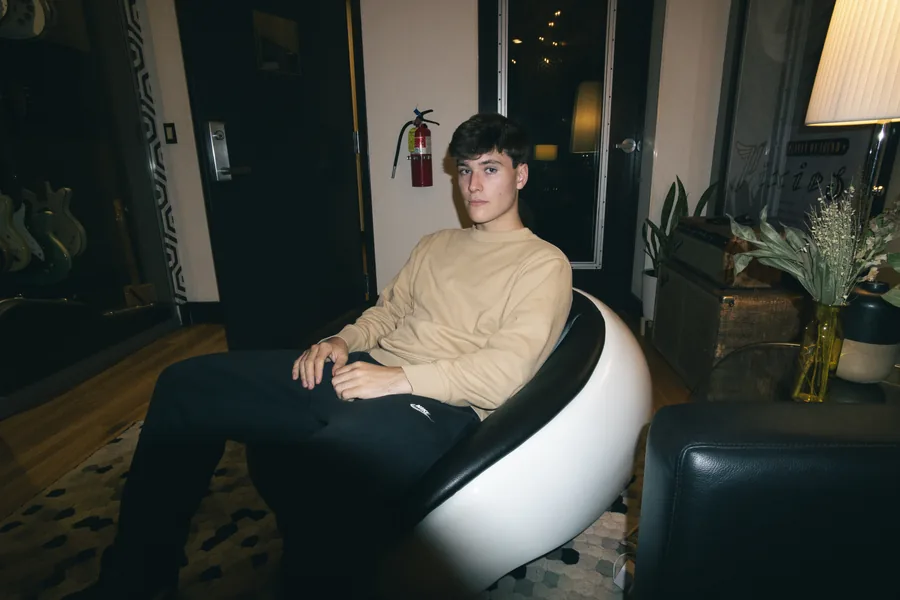 Seated in a white chair at the end of a studio hallway